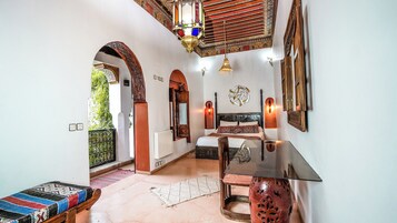A room with a bed, a table, and a bench. There are decorative wall sconces and a hanging lantern.