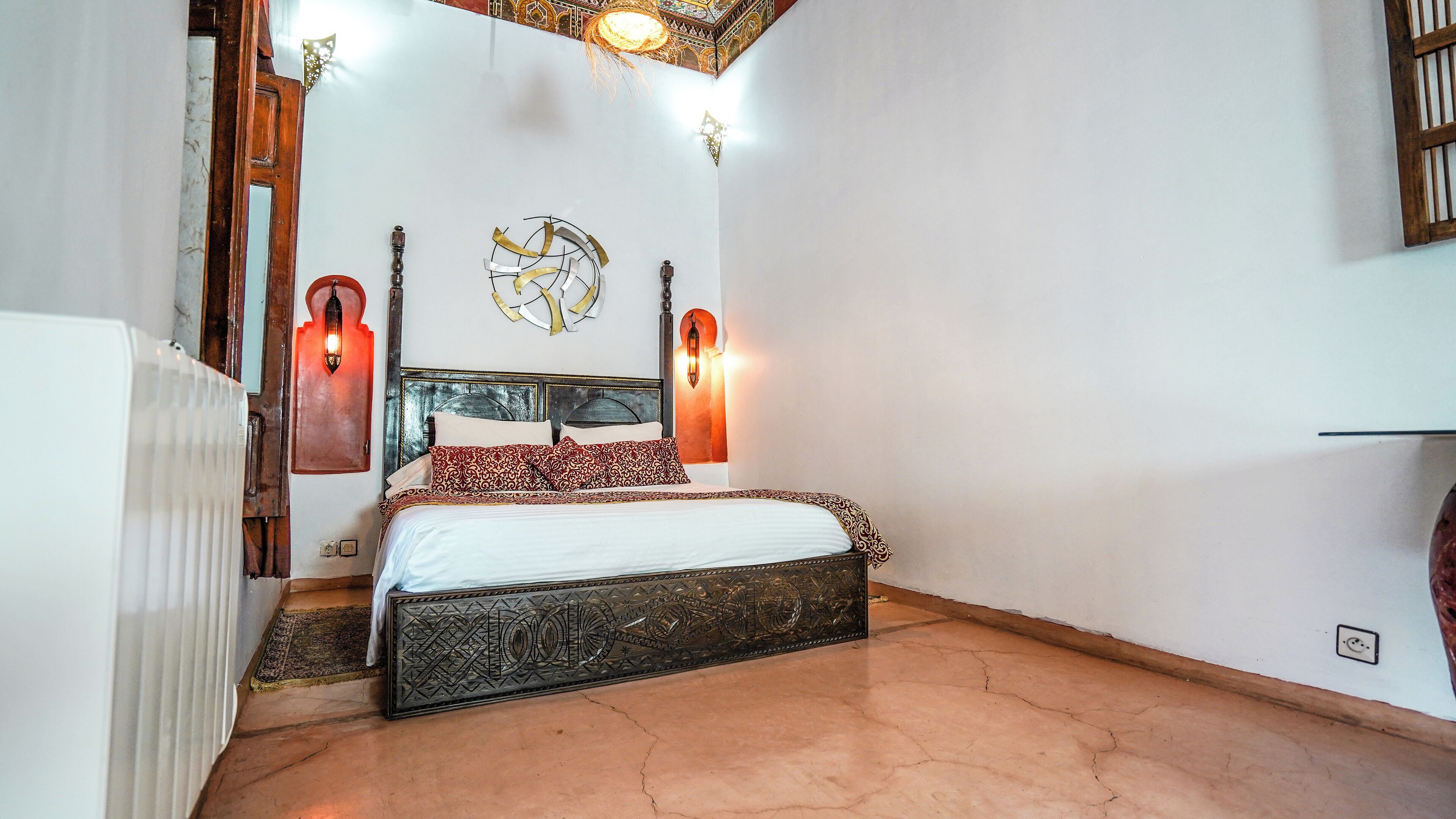 Un dormitorio con cama, dos lámparas de pared, un adorno en la pared y un radiador.