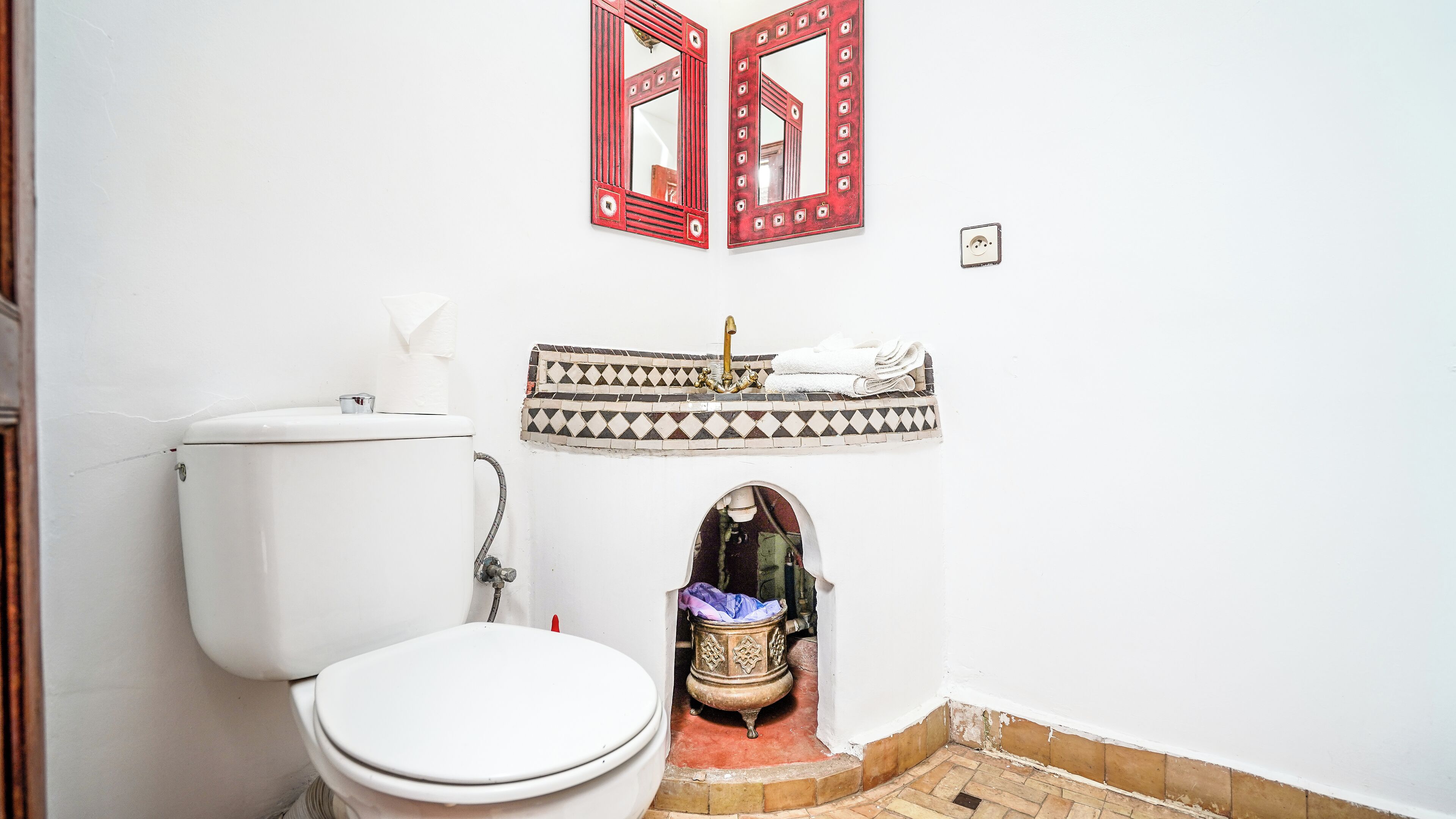 A bathroom with a white toilet, a sink with a decorative basin, and two mirrors with red frames.