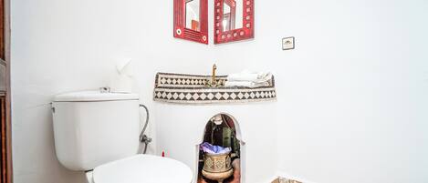 A bathroom with a white toilet, a sink with a decorative basin, and two mirrors with red frames.