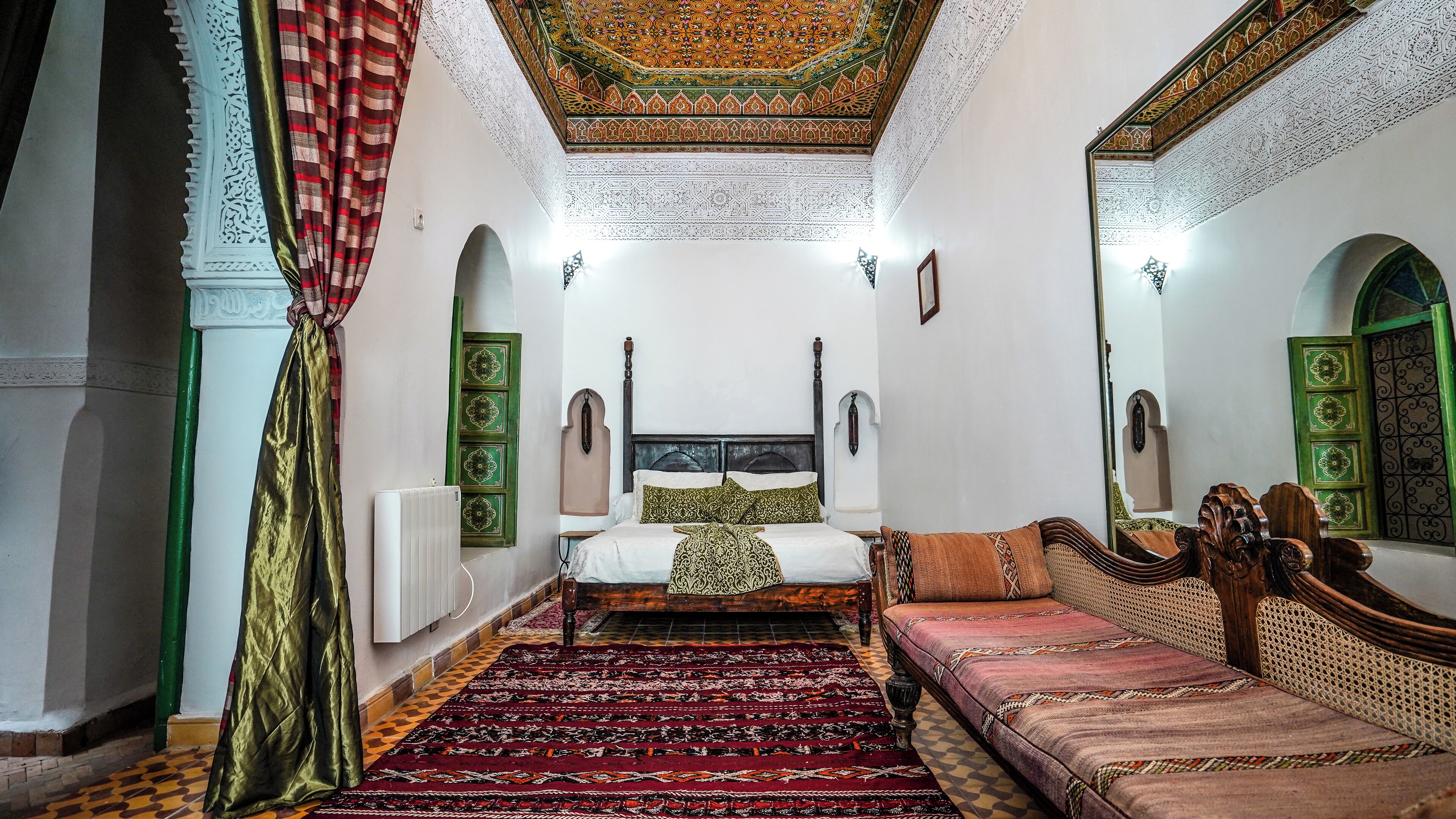 Een klassieke kamer met een bed, een slaapbank, een kamerbreed tapijt en decoratieve ontwerpen aan het plafond en de muren.