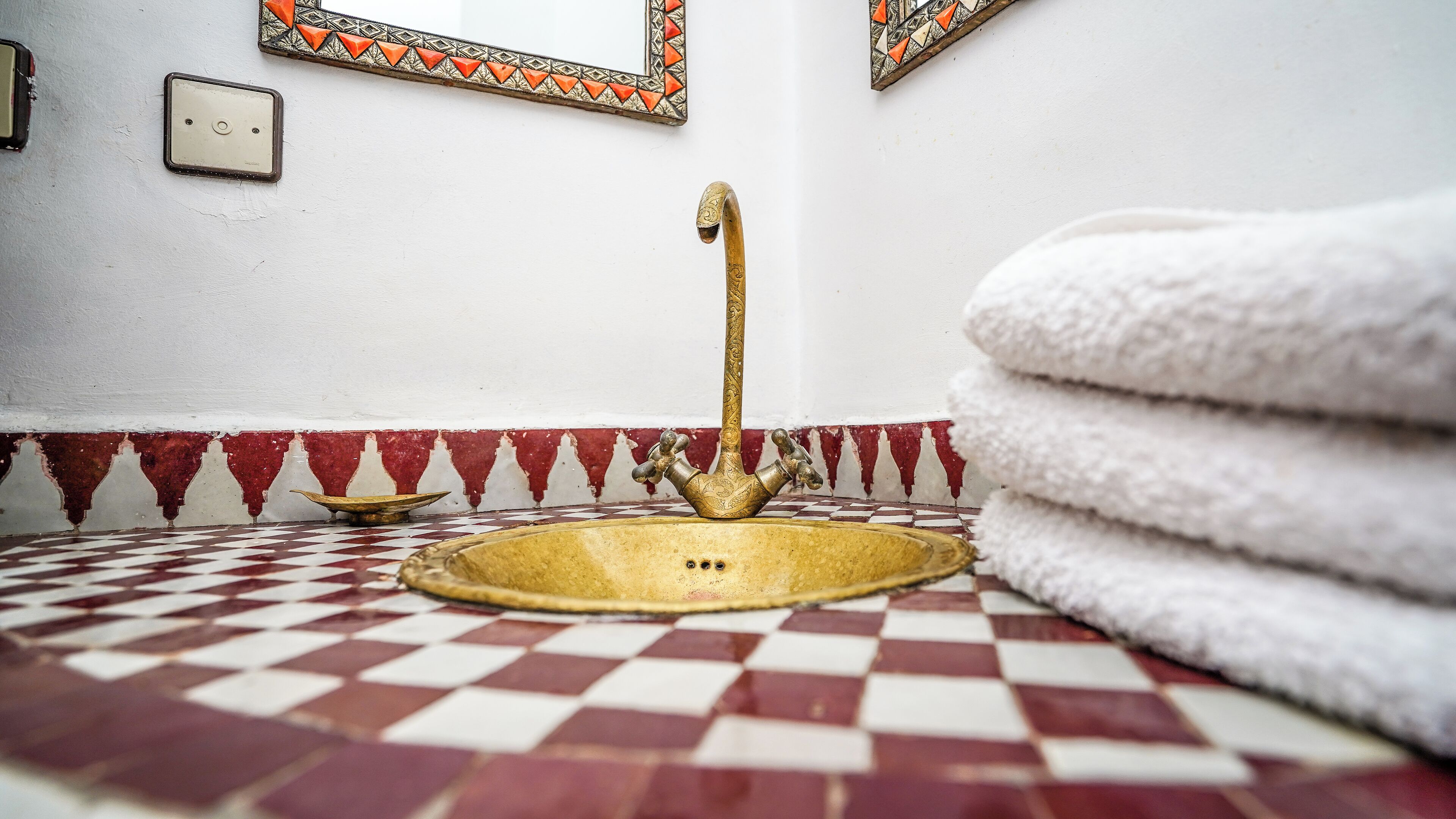 A bathroom with a checkered floor, a golden sink with a curved spout, and a stack of white towels.
