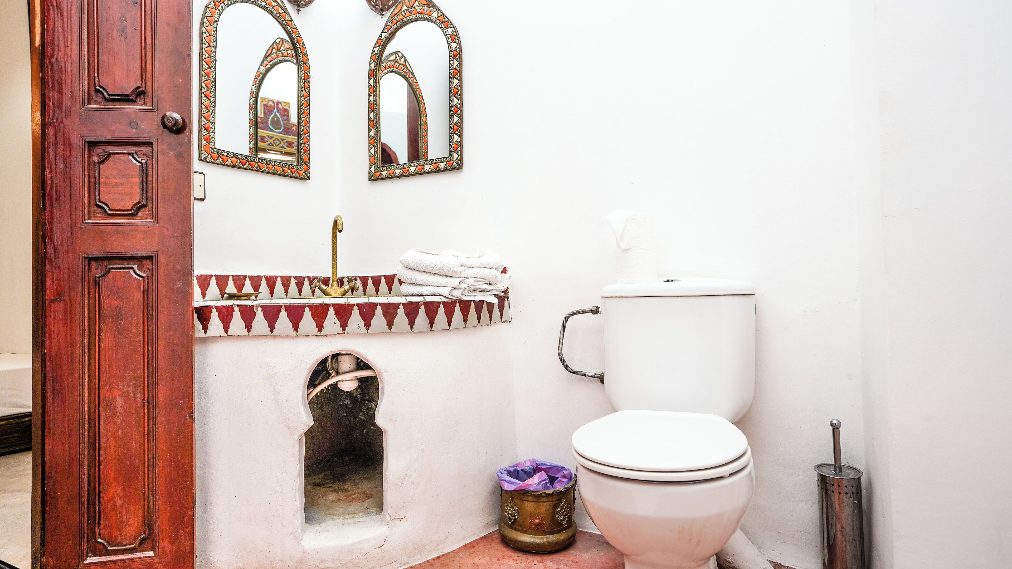 A bathroom with a white toilet, a sink with a decorative tile border, and two wall-mounted mirrors.