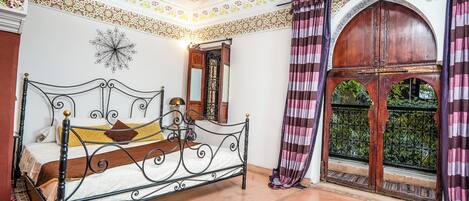 A traditional room with a bed, a window with a view, and decorative ceiling patterns.