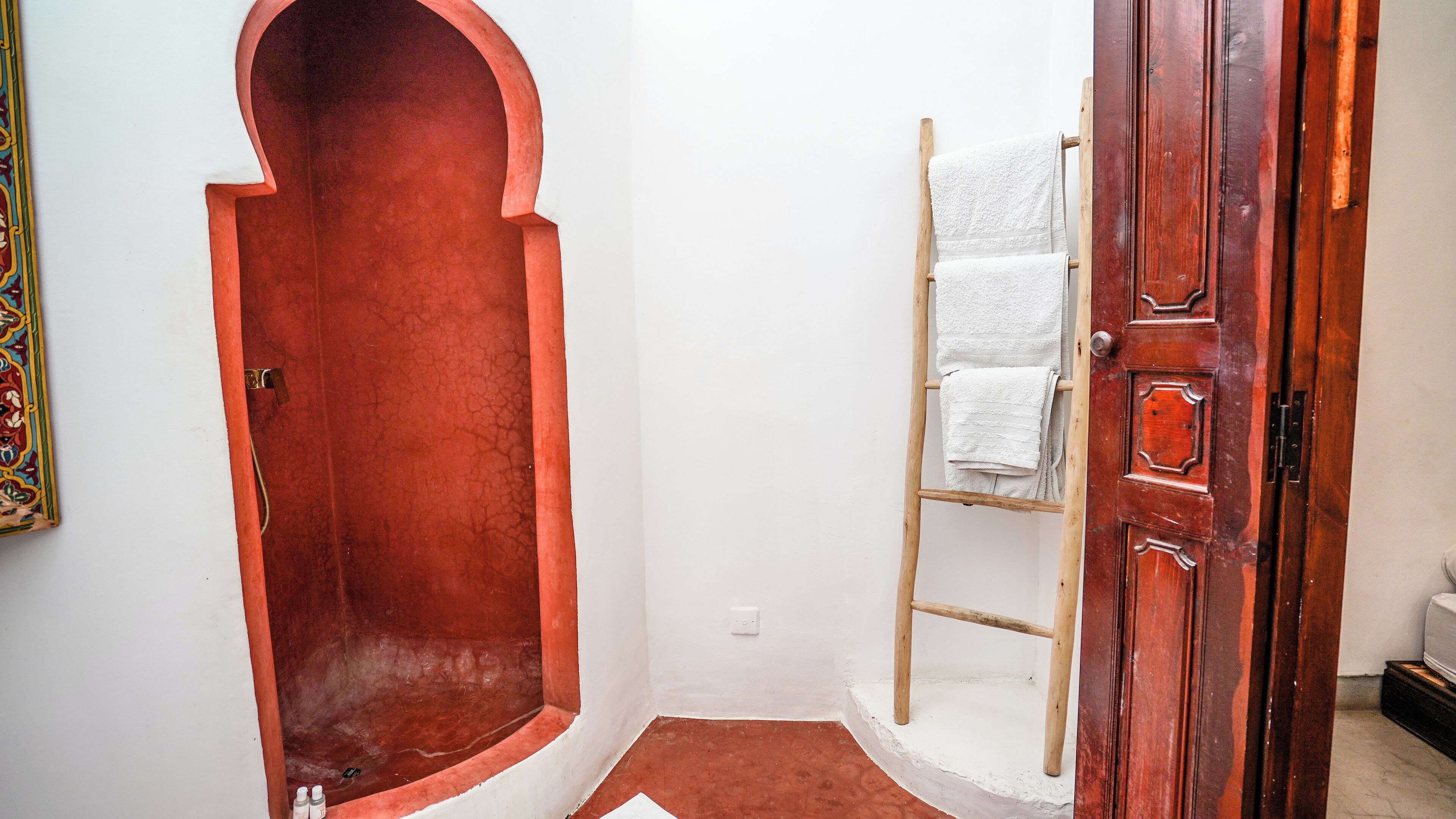 Een badkamer met een vloer van rode tegels, een houten trapje en een witte handdoekhouder.