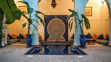 A traditional Moroccan interior with a central fountain, ornate tile work, and seating areas with cushions.