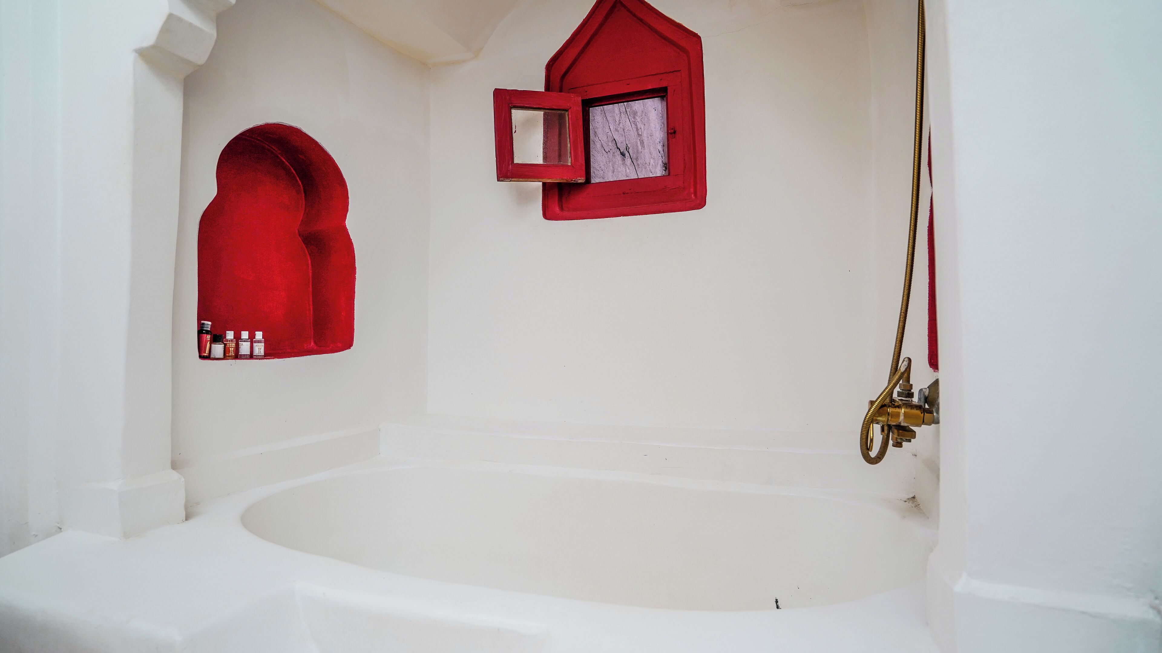 A white bathtub with a showerhead, a red window, and a red door.