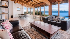 Un'ampia zona giorno con soffitto in legno, ampie finestre con vista sulle montagne, un divano in pelle e un tavolino da caffè.