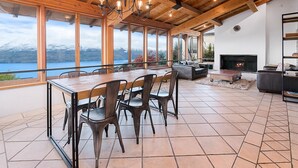 Un'ampia zona giorno con un grande soffitto in legno, un camino e vista su un lago e montagne.