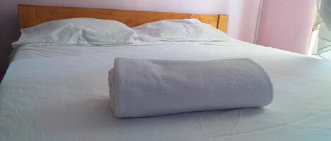 Una cama bien hecha con sábanas y almohadas blancas, un cabecero de madera y una ventana con cortinas.