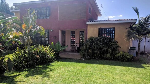 A two-story house with a well-maintained lawn and tropical plants.