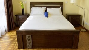 A large bed with a wooden headboard, two bedside tables, a floor lamp, and a vase with plants.