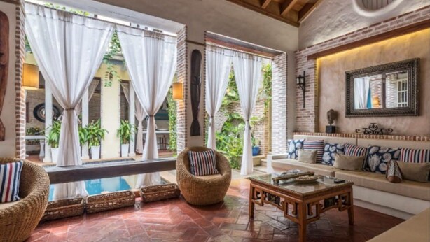 A spacious living area with a brick wall, a sofa set, a wicker chair, and a coffee table.