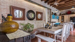 A rustic dining area with a brick wall, wooden beams, and a long table with white chairs.
