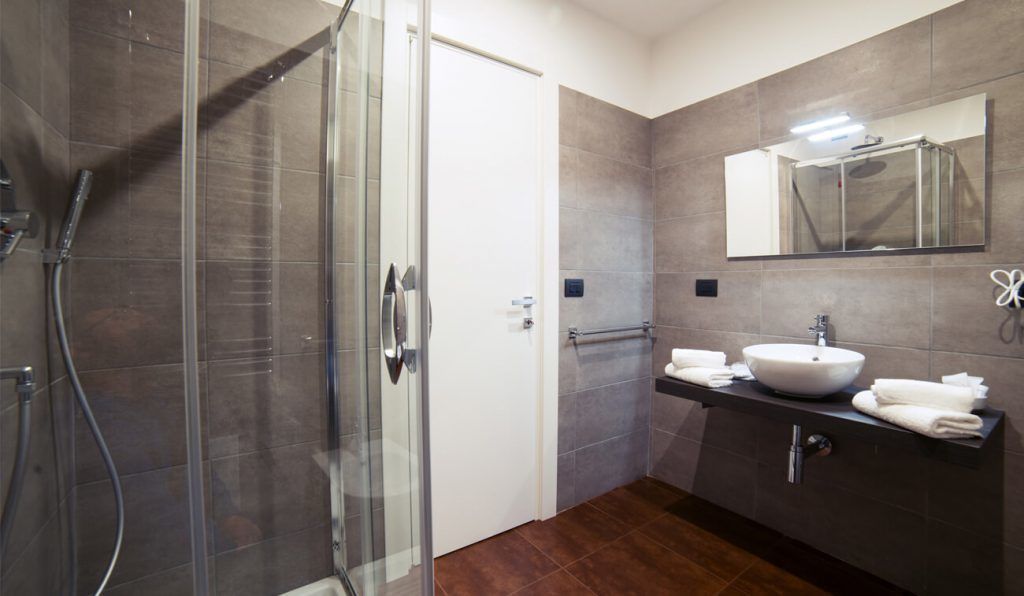 Une salle de bain moderne dotée d’une douche à parois de verre, d’un grand miroir et d’un meuble-lavabo avec un évier et un porte-serviettes.