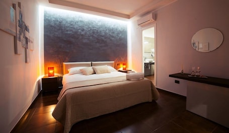 A modern bedroom with a large bed, bedside lamps, a small bedside table, and a wall-mounted mirror.