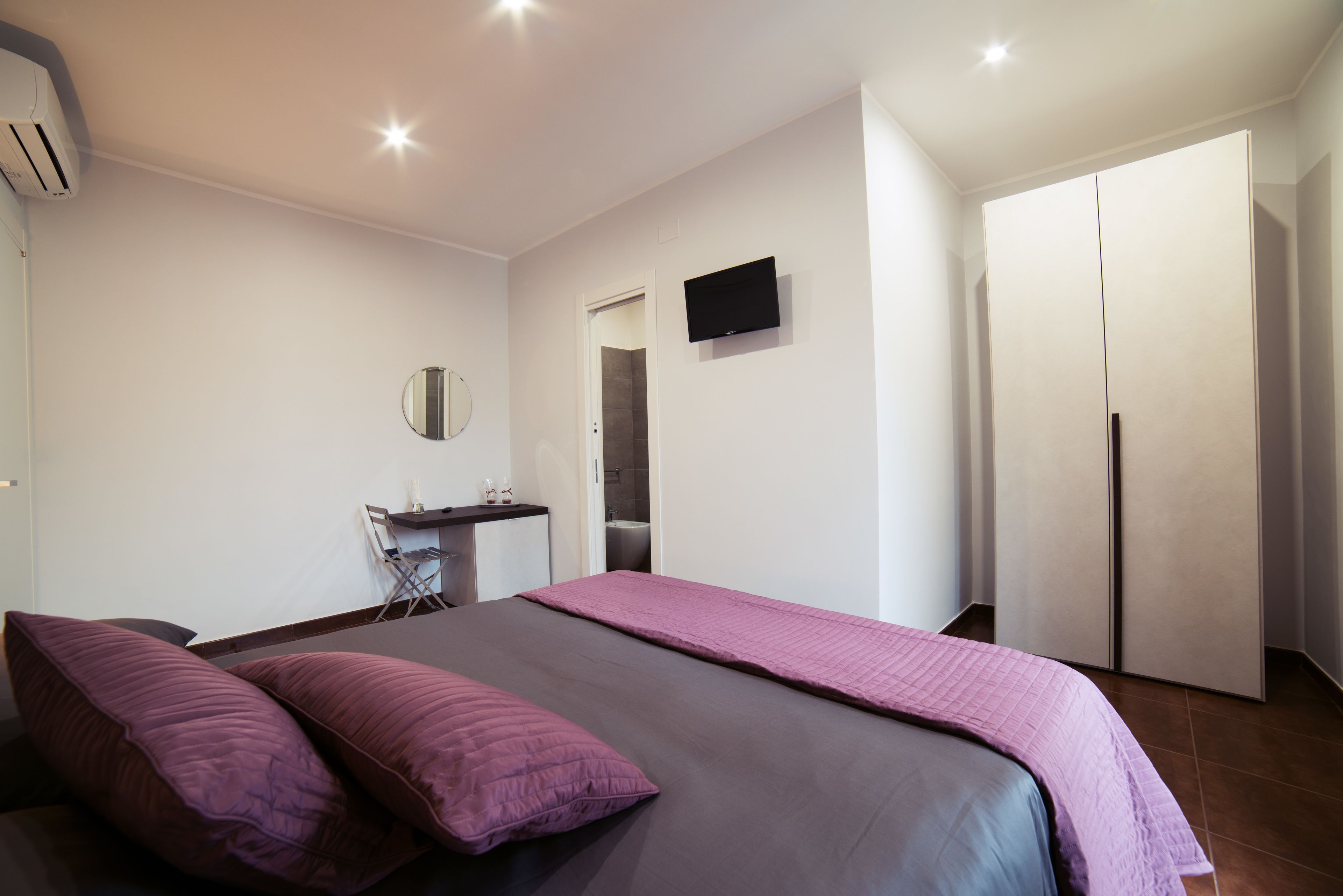 Un dormitorio con una cama, dos almohadas, un televisor, un armario y un espejo.