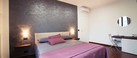 Un dormitorio moderno con una cama grande, una mesita de noche, un escritorio pequeño y un espejo redondo en la pared.