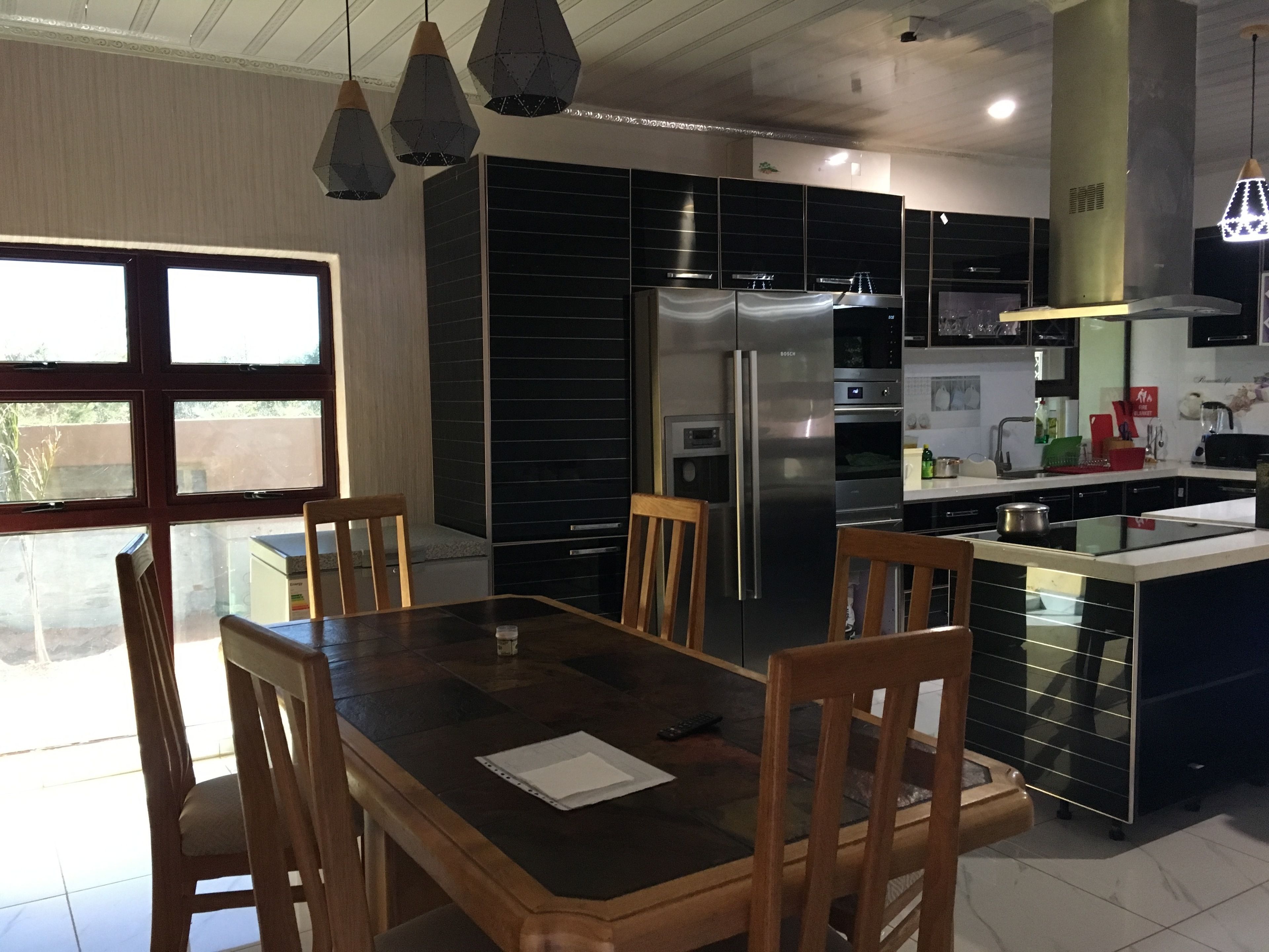 A modern kitchen with a central island, stainless steel appliances, and a dining area with wooden chairs and a table.