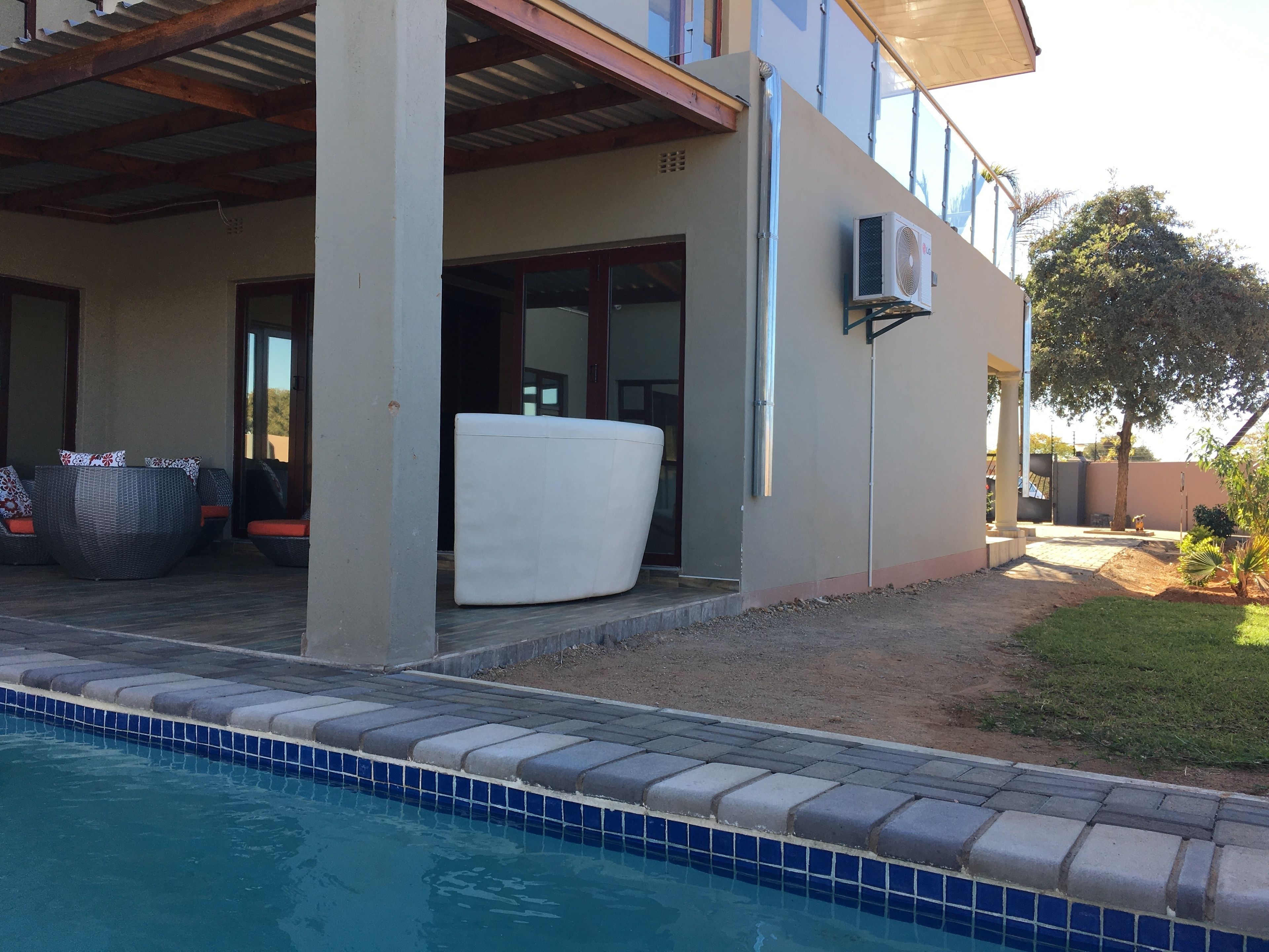 A poolside area with a covered patio, outdoor seating, and a large air conditioning unit mounted on the wall.