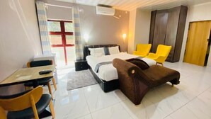A hotel room with a bed, a desk with chairs, a sofa, and a wardrobe. - Kanyi Guest House (Palapye)