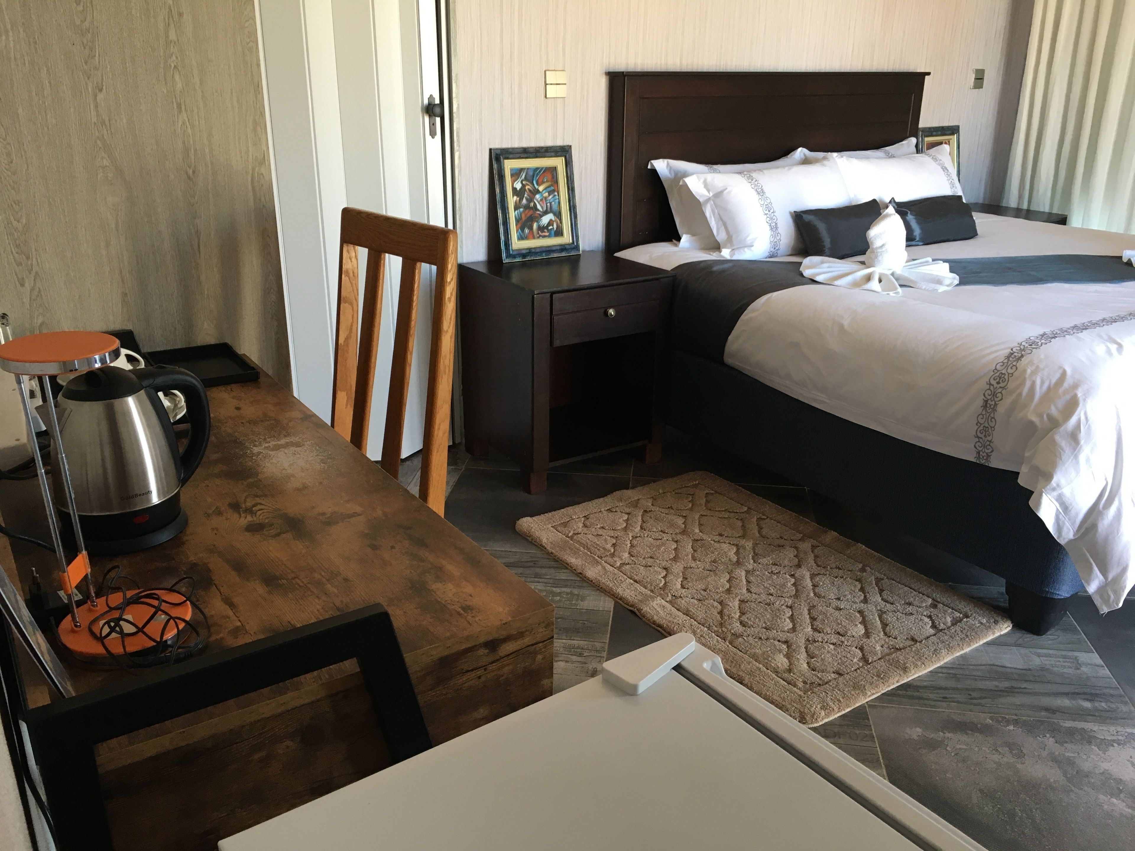 A hotel room with a bed, a desk, a chair, a coffee maker, and a rug.
