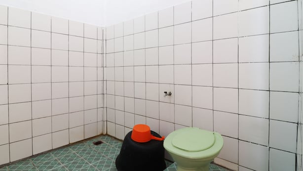 Un baño pequeño con paredes de azulejos, un inodoro y un recipiente negro con tapa naranja.