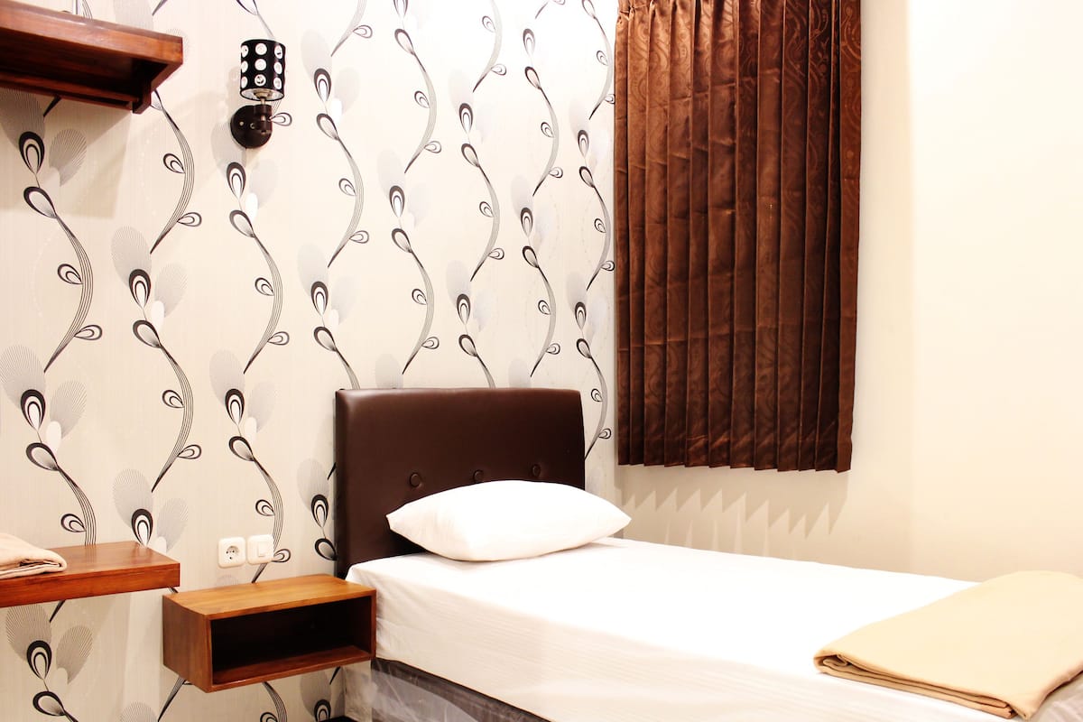 A neatly made bed with a white pillow, a wooden nightstand, and a wall-mounted light fixture.
