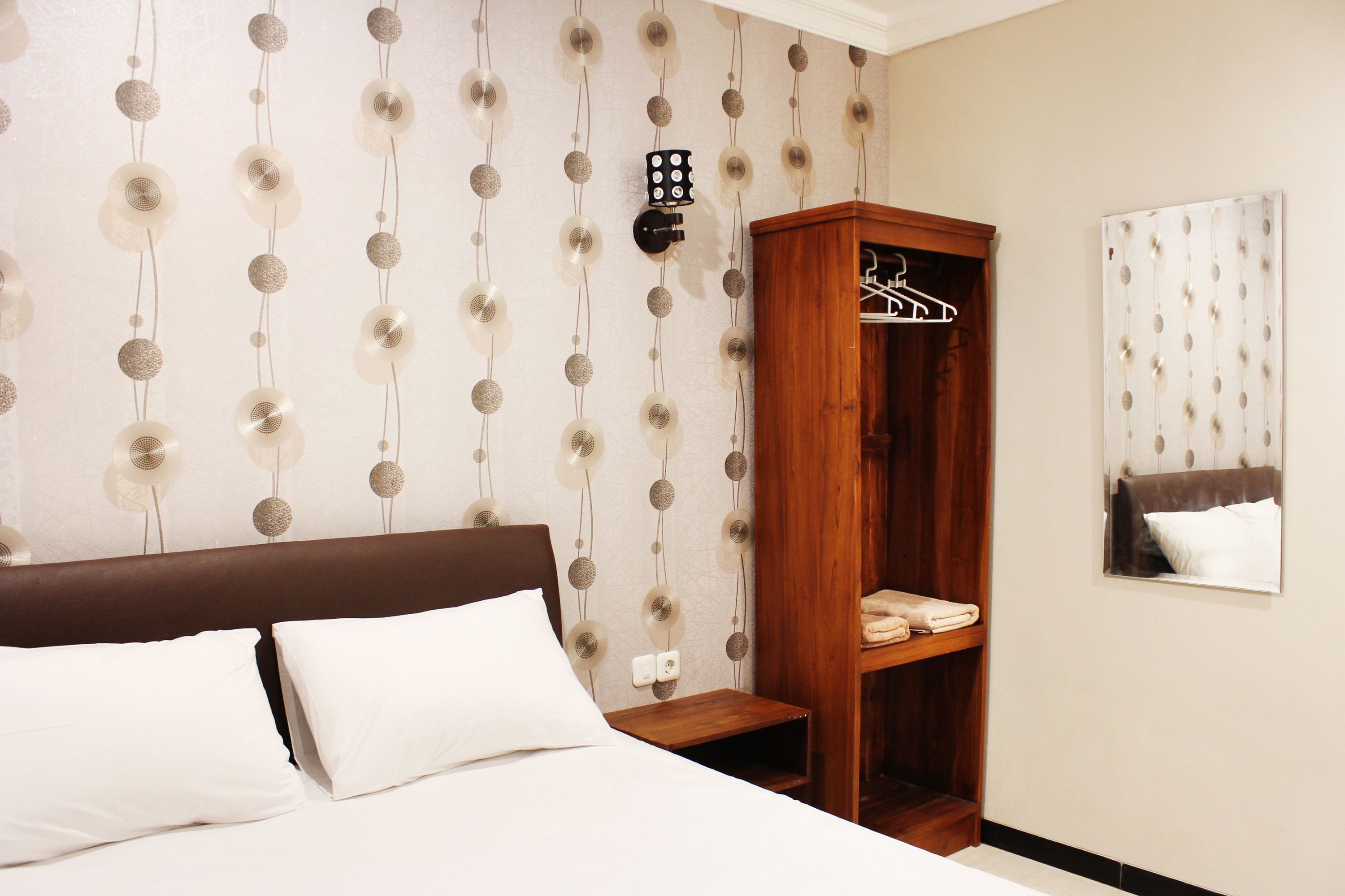 A hotel room with a bed, a wooden wardrobe, and a mirror on the wall.