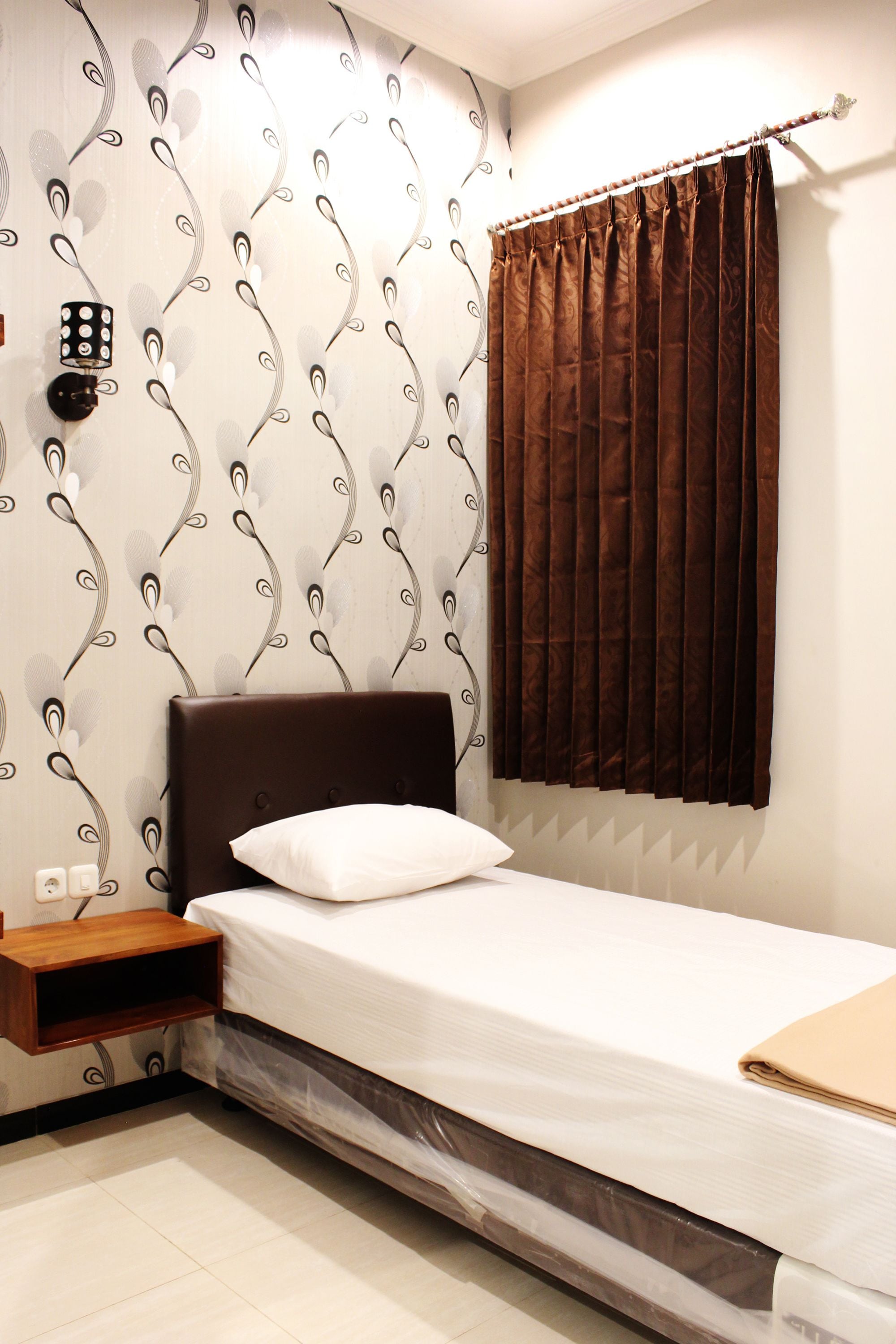 A neatly made bed with a white pillow, a wooden nightstand, and a wall with a decorative pattern.
