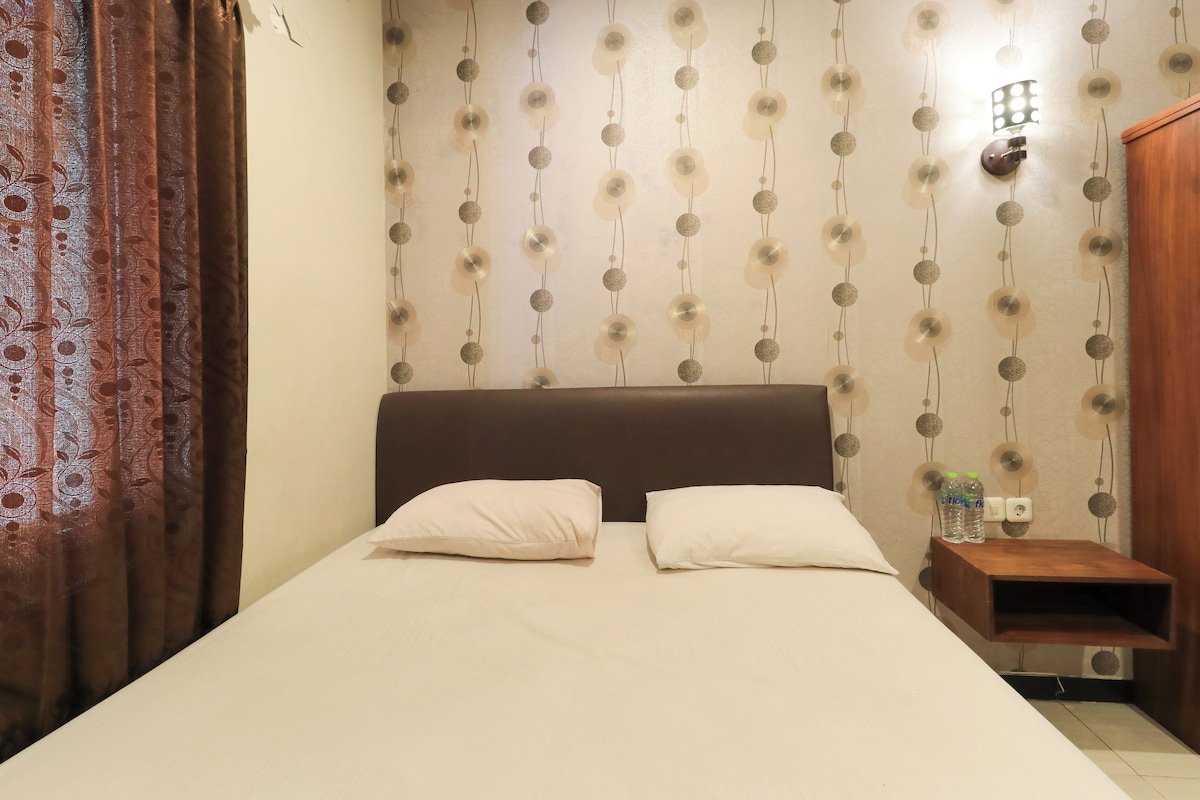 A neatly made bed with two pillows, a wooden headboard, and a wall with a patterned wallpaper.