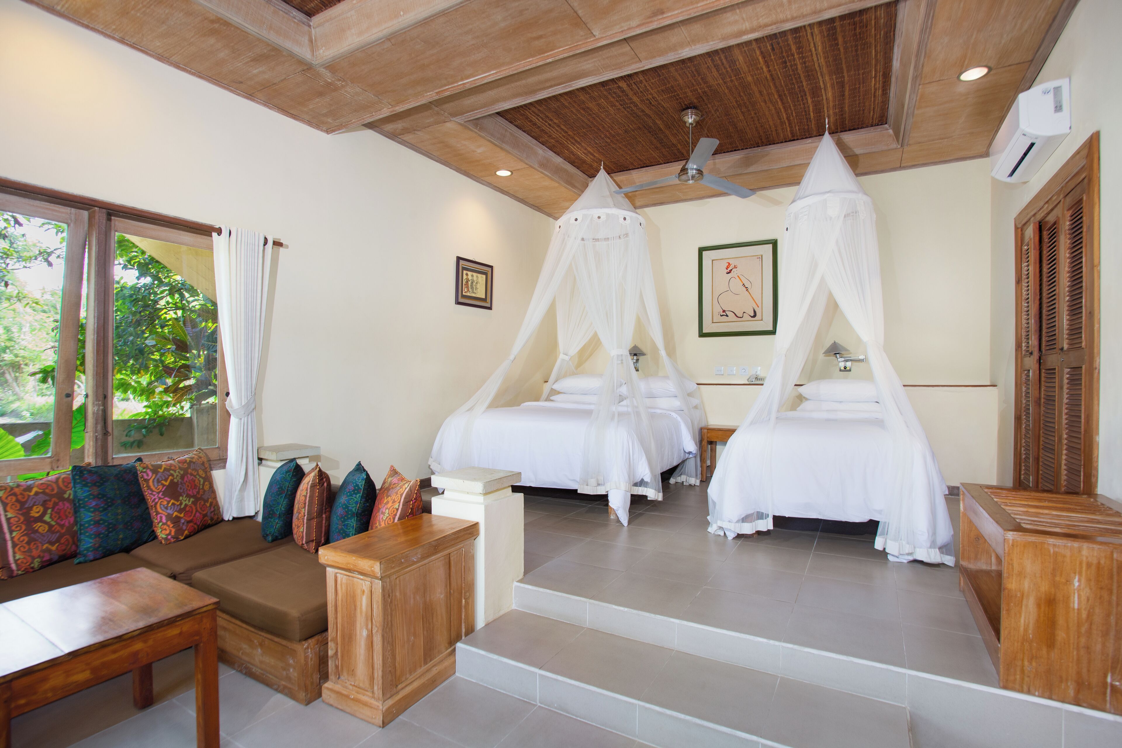 A bedroom with two beds, a sofa, a wooden table, and a ceiling fan.