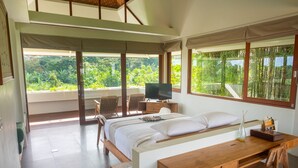 A room with a bed, a desk, a TV, and large windows overlooking greenery. - Tegal Sari Accomodation (Ubud)