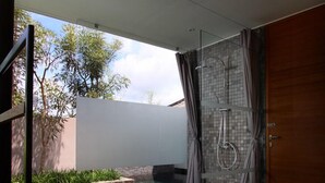 A modern bathroom with a glass shower enclosure, a small pool, and a wooden door. - Tegal Sari Accomodation (Ubud)