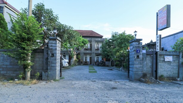 A hotel entrance with a paved driveway leading to a building with a red roof. - Hotel Warta Putra (Denpasar)