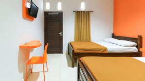 A room with two beds, a desk with a chair, a TV mounted on an orange panel, and a door with a curtain. - Hotel Warta Putra (Denpasar)