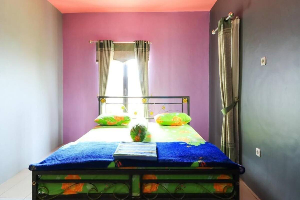 A bed with a blue bedspread and floral pillows, a window with curtains, and a metal bed frame.