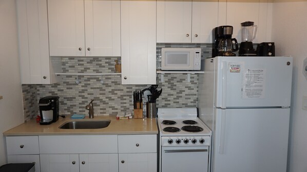 A compact kitchen with white cabinets, a microwave, a coffee maker, a stove, and a refrigerator. - GROUND FLOOR STUDIO ~ BEACHSIDE condo with a kitchen, walkout to pool.FN #401 (St Pete Beach)