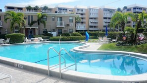 A swimming pool with a 5 1/2 ft depth, surrounded by lounge chairs and a building with balconies. - GROUND FLOOR STUDIO ~ BEACHSIDE condo with a kitchen, walkout to pool.FN #401 (St Pete Beach)