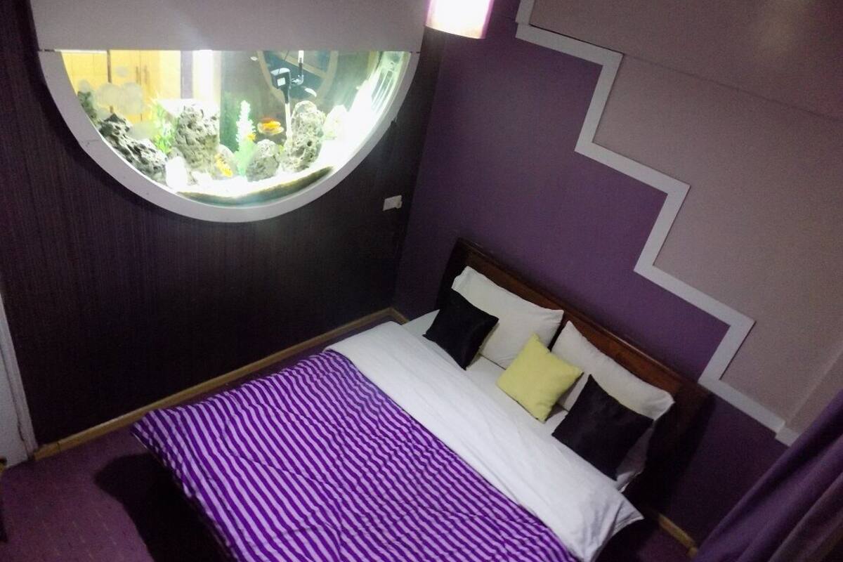 Quarto com cama, janela redonda e vista para um aquário.