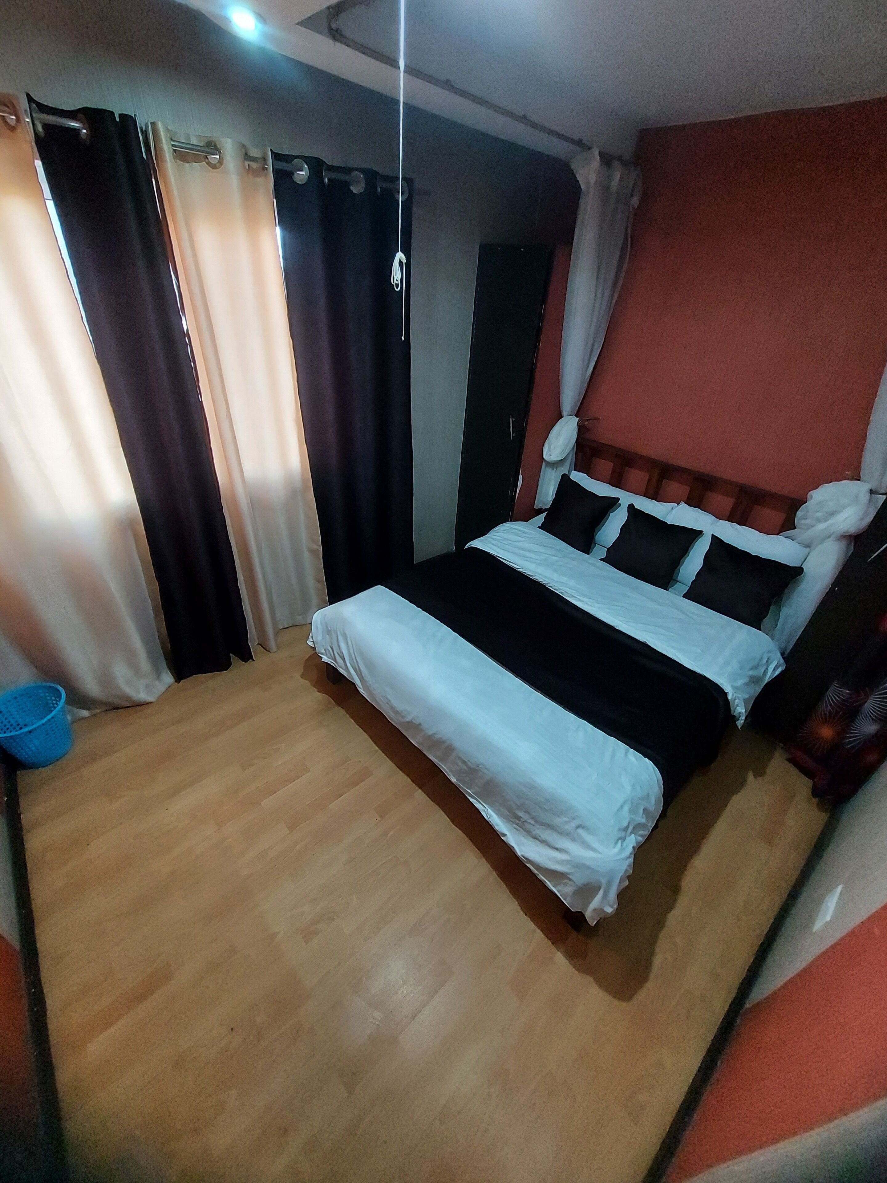 Een slaapkamer met een houten vloer, een bed met zwart-witte beddengoed en gordijnen voor de ramen.