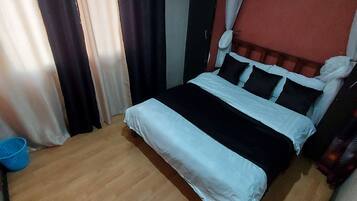Een slaapkamer met een houten vloer, een bed met zwart-witte beddengoed en gordijnen voor de ramen.