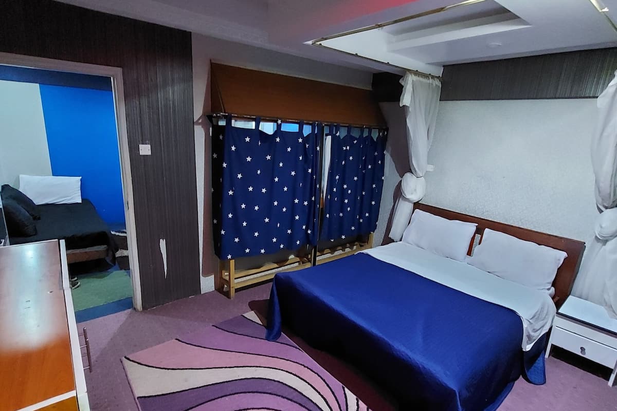 Quarto de hotel com cama, mesa de cabeceira, cômoda e área de chuveiro.