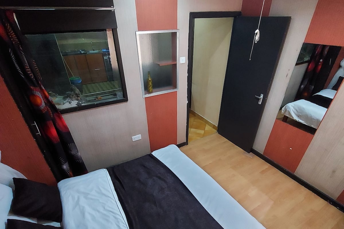 Um quarto com cama, janela, porta e uma pequena estante.