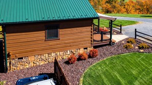 Une cabane rustique en rondins de bois, avec un toit en métal vert, des fondations en pierre et une véranda dotée d’une balustrade.