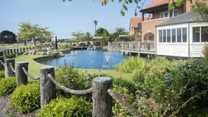 A garden with a pond, a wooden fence, and a building with a balcony. - Monaco Resort - Home to Compass Cottage (Monaco)