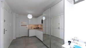 A modern kitchen with white cabinets, a central island, and a large mirror. - Cozy Studio | 400 m to the Beach, Gym, Balcony (Kołobrzeg)