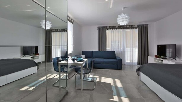 A modern hotel room with a bed, a sofa, a dining table, and a TV. - Cozy Studio | 400 m to the Beach, Gym, Balcony (Kołobrzeg)
