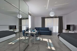 A modern hotel room with a bed, a sofa, a dining table, and a TV.