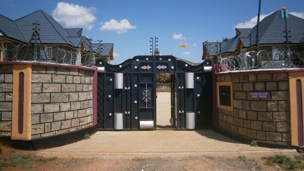 A gated entrance with a black gate, stone walls, and a clear sky. - Elgon Village Guest House (Eldoret)